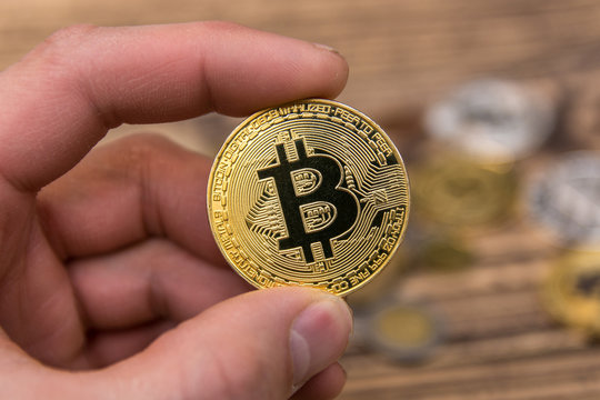  bitcoin holding in man&rsquo;s fingers on old wooden background