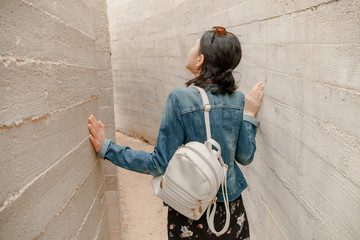 Attractive young woman standing between concrete walls. Caucasian girl in casual jeans looks up.