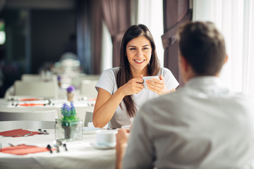 Smiling woman on a date in a restaurant,having a conversation over a meal in hotel.Cheerful female customer drinking coffee with a partner.Positive emotions,love,affection.Public place behave manners