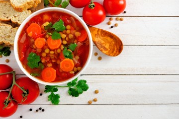 Homemade tomato, lentil soup, above view corner border with copy space on a white wood background