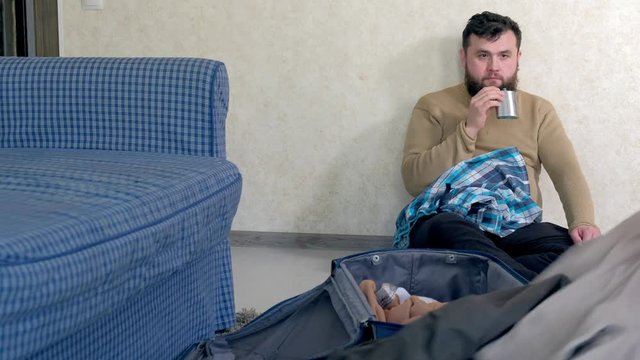 Disappointed,crying and beaten young woman packing her clothing in the suitcase, drunken, drinks from a metal flask,he takes out and throws her stuff from the bag,conceptual scene.