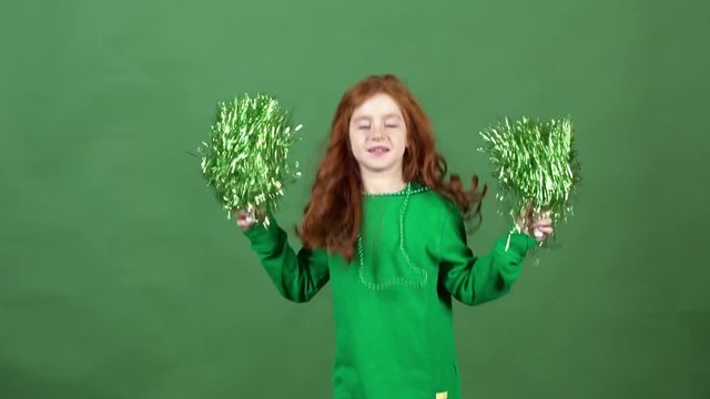 Girl red hair celebrating saint patrick's day green wall background playing with pom poms