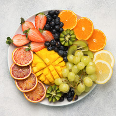 Colourful fruits and berries in rainbow colours, on a plate, strawberries, mango, grapes, bananas, grapefruit on the off white table, square, copy space for text, selective focus