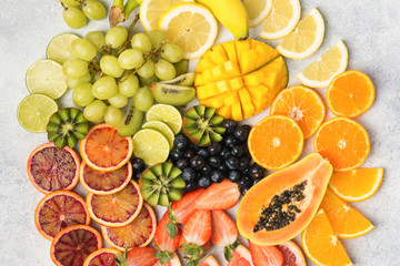 Top view of healthy fruits in rainbow colours, strawberries, mango, grapes, bananas, grapefruit on the off white table, copy space for text, selective focus