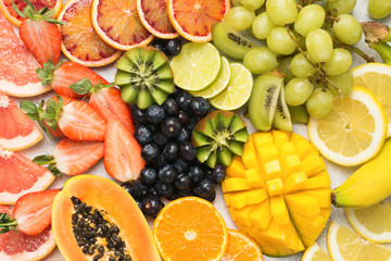 Healthy colourful fruits in rainbow colours, strawberries, mango, grapes, bananas, grapefruit on the off white table, top view, selective focus
