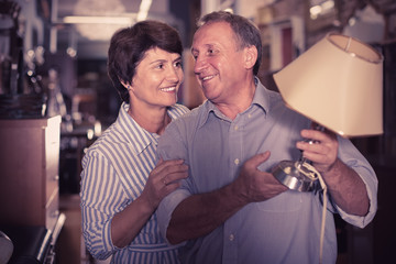 positive mature couple is shopping the old lamp in the antique store