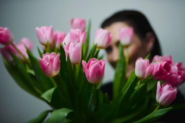 Portrait of attractive young woman with tulips is standing in light room and smiling. Happy international women's day! Celebrating 8th of March.