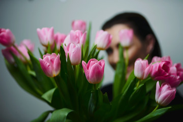 Portrait of attractive young woman with tulips is standing in light room and smiling. Happy international women's day! Celebrating 8th of March.