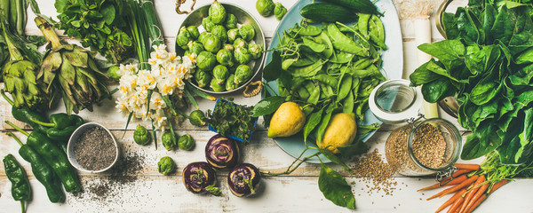 Ingrédients de cuisine végétalienne saine de printemps. Mise à plat de légumes, fruits, graines, germes, fleurs, verts sur fond de bois blanc, vue de dessus. Manger propre, concept de régime alimentaire