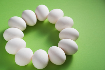 White chicken eggs laid out in an circle on green background