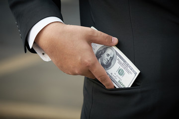 Businessman wearing a black suit. Hold a dollar bill. Put in a pocket The bracelets of the business.using as background business concept with copy space for your text or design.