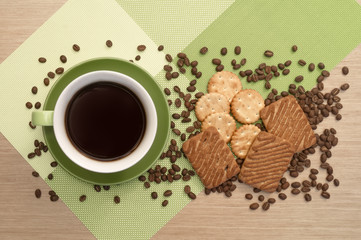 Green cup of coffee on the table and biscuit and beans. View from top