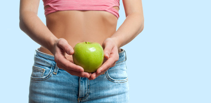 Diet concept. Beautiful woman with slim waist is holding apple on pastel background