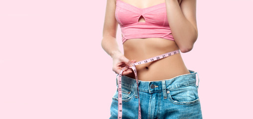 Woman is measuring waist after weight loss on faded pastel background