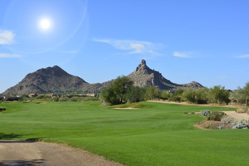 Sun shining over a green golf fairway with mountains and a blue sky © jessicakirsh