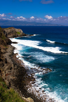 Volcanic rock, surf, and shades of the blue Pacific Ocean on the Maui coast, with the island of Molokai in the background