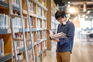Young Asian man university student reading book in library, education research and self learning in...