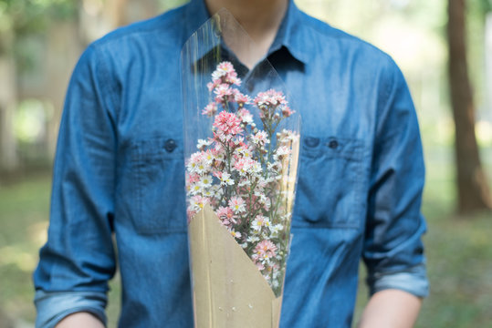 half body of man in blue jean shirt hand hold flower in middle cheast.