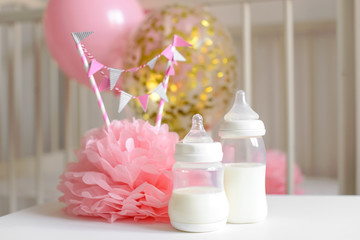 Obraz na płótnie Canvas Baby bottles with breast milk with various festive paper decor and balloons in front of baby bedroom. It's a girl or baby birthday celebration concept. Baby shower concept.