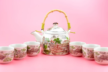 Teapot with cups on a pink background.