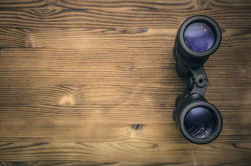 Binoculars on wooden table background with copy space for treasure map for example. Find and search concept.