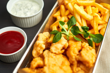 chicken nuggets with french fries and different sauces on wooden board,