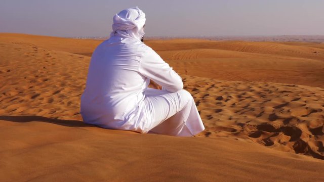 lonely arab man in white kandura sitting in hot sandy desert