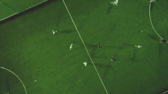 Aerial football match play. Clip. Aerial shot Two teams playing ball in football outdoors, top view. Football game outdoors, green field with markings, players running around with a ball