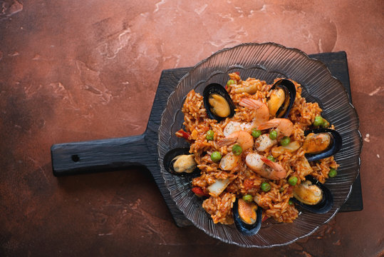 Plate with seafood paella on a black wooden serving board, top view on a fire warm rusty metal background, copyspace