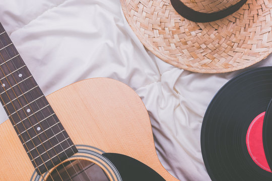acoustic guitar, record & hat on white bed. relaxation and travelling concept