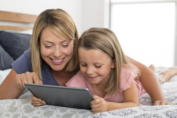 Fototapeta na wymiar blond Caucasian mother lying on bed with her young sweet 7 years old daughter using internet on digital internet tablet pad together at home