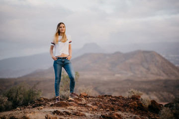 Beautiful girl watches straight and poses in the mountains on the sunrise. Tenerife