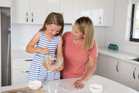 blond woman cooking and baking happy together with sweet adorable mini chef little girl at home kitchen in mother and daughter love