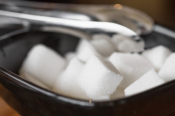Fototapeta na wymiar Sugar cubes in the sugar bowl with sugar tongs. Closeup, selective focus