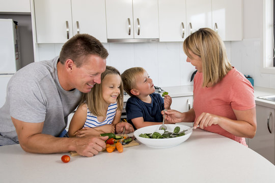 young attractive couple mother and father preparing salad together with little son and young beautiful daughter in healthy vegetable nutrition