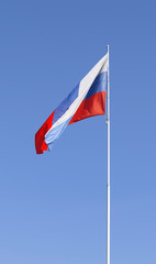 The national flag of Russia fluttering on a flagstaff against the background of the clear blue sky