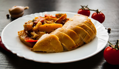Fried chicken breast with carrots, onions and potatoes served on a white plate on dark wooden background