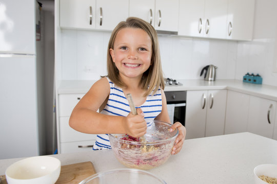 young beautiful and adorable girl 6 or 7 years old cooking and baking at home kitchen preparing strawberry cake with bowl smiling happy and confident