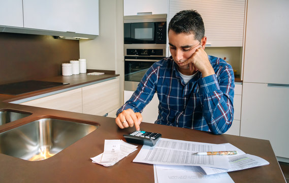 Young Man Checking Bills Of His House In The Kitchen