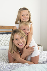 young blond Caucasian woman lying on bed together with her little sweet 3 and 7 years old son and daughter laughing playing happy at home