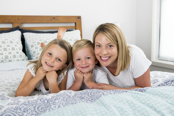 young blond Caucasian woman lying on bed together with her little sweet 3 and 7 years old son and daughter smiling playful and happy