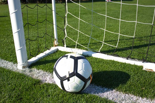 White soccer ball in the gate on a green grassy football field