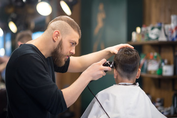 the young man the hairdresser cuts the schoolboy in hairdressing salon