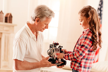 Look what Ive got. Side view on calm grandfather and girl focusing their attention on a robot toy while both examining the robotic machine.