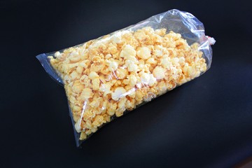 Sweet popcorn in transparent plastic bag, black background