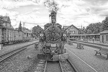 Historic steam powered railway train at train station in black and white