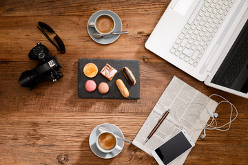 Fototapeta na wymiar above view still life of two espresso coffee macaroons and french pastries on a rustic wooden tables with a computer, smartphone earphone camera and newspaper