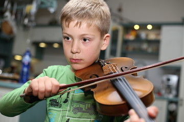 Blond small kid playing violin in the kitchen