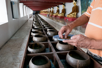 Give coin in alms bowl, a man put a Baht coin in a monk bowl for making merit or donation, Buddhism Thai people donating money in row of bowl for temple in Cultural of tourism in Thailand Travel.