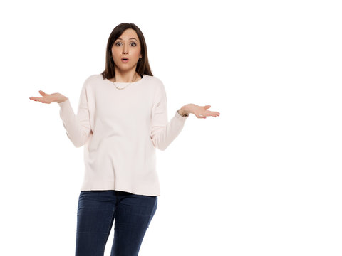 Young woman in jeans, blouse and snekaers with questionable gesture on white backgeound